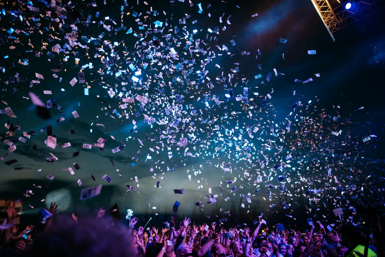 Crowd with hands up facing a lit festival stage at night