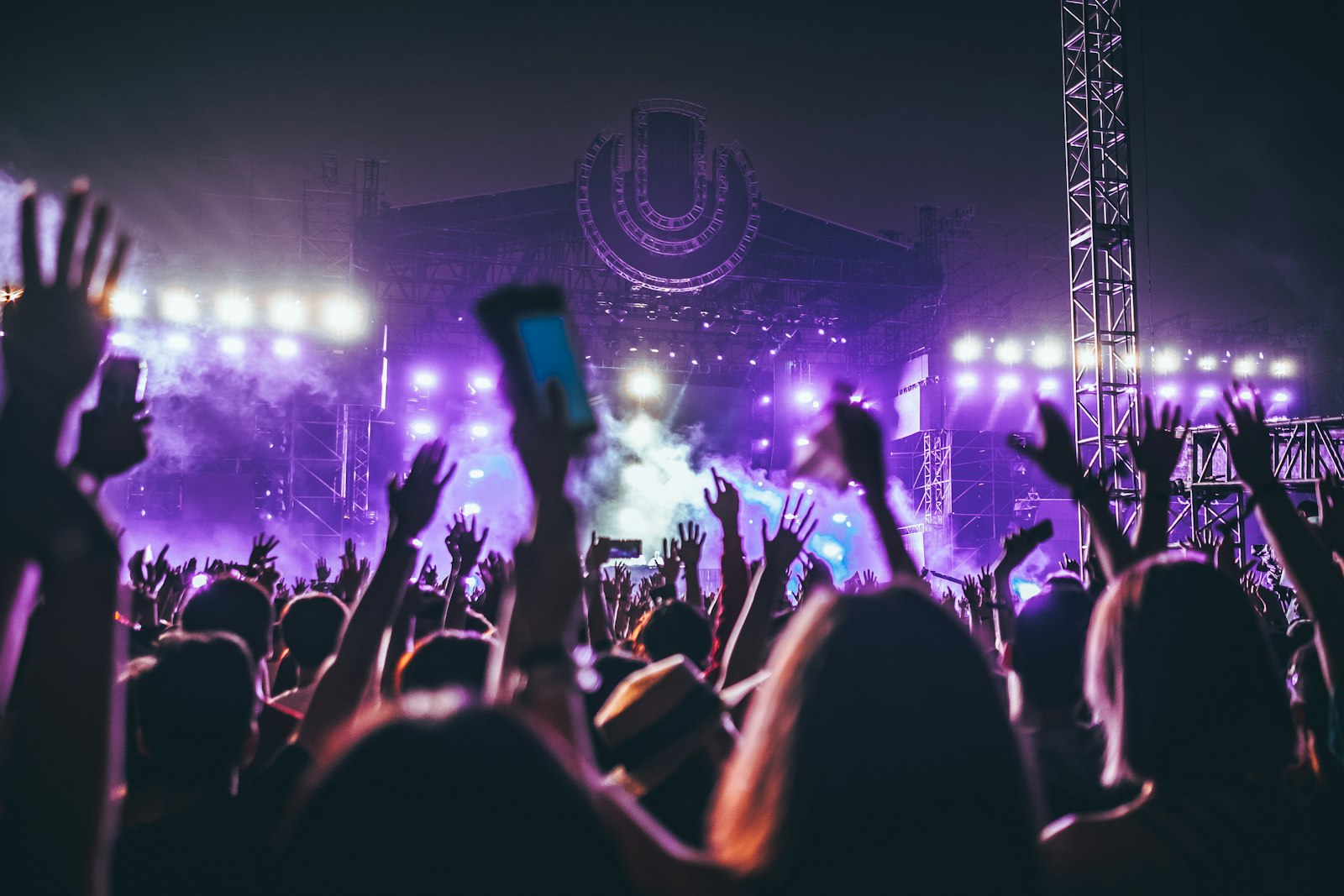 Crowd with hands raised at a music festival with colorful stage lights